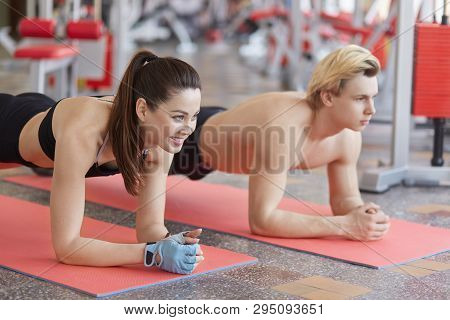 Side View Of Muscular Couple Doing Planking Exercises, Look Straight Ahead, Being In Good Mood, Work