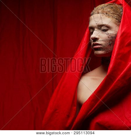 Portrait Of A Young Strange Ginger Girl In Red Wrinkled Cape Over Red Curtain Background. Wire On A 