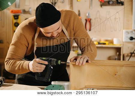 Portrait Of Working Handsome Middle Aged Bearded Carpenter In A Watch Cap. He Is Making Furniture On