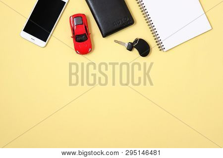Car Rental Or Sharing Concept. Smartphone, Driver License, Toy Car And Automobile Key On Yellow Back