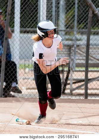 Red Haired High School Softball Player Hustling Up The First Base Line After Hitting The Ball.