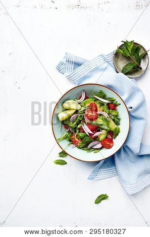Mixed salad made with cherry tomatoes, arugula, red onion, avocado and mint leaves. Healthy home made food. Flat lay. Copy space