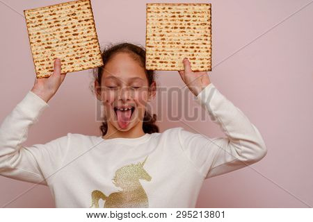 Portrait Of The Cute Teenager Girl Holding Matzah And Shows Tongue. Jewish Child Eating Matzo Unleav