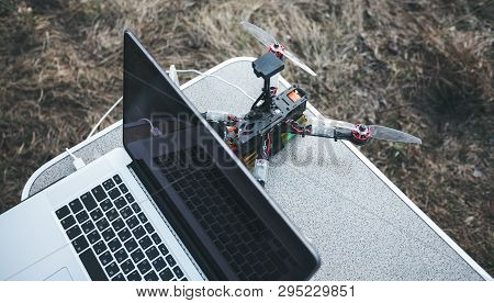 Fpv Drone Lies On The Table Near The Laptop And Control Panel. The Pilot Sets Up His Racing Drone Be