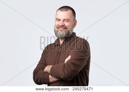 Confident Senior Man With Beard In Brown T-shirt Crossing Hands On Chest And Looking At Camera