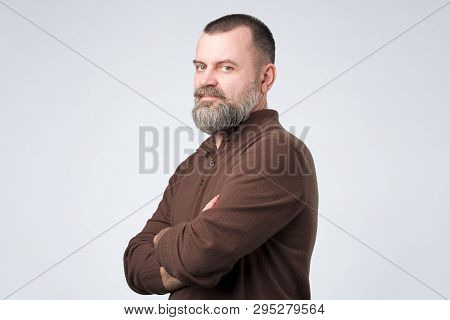 Confident Senior Man With Beard In Brown T-shirt Crossing Hands On Chest And Looking At Camera