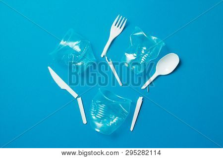 White Broken Single-use Plastic Knives, Spoons, Forks And Plastic Drink Straws On A Blue Background.