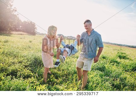Mother And Father Swinging Son In Sunnny Summer Day