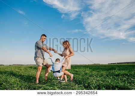Mother And Father Swinging Son In Sunnny Summer Day