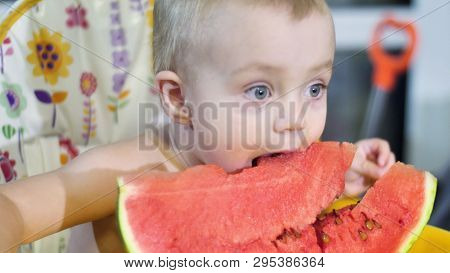 Little Baby Eating A Piece Of Watermelon At The Kids Table On The Kitchen And Then Smiling Shakes Hi