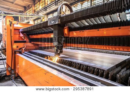 Huge industrial machine processing metallic workpiece or sheet with stream of cutting beams inside contemporary factory