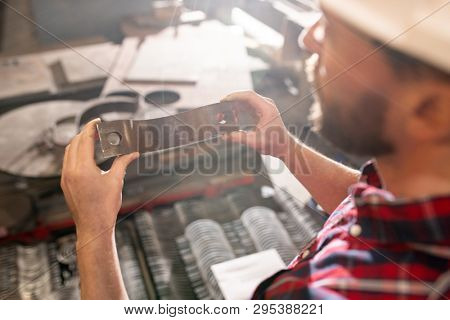 Young contemporary professional engineer or technician holding metallic detail while choosing one for industrial machine