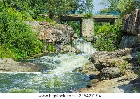 Small Waterfall On River Flowing From Under A Stone Bridge