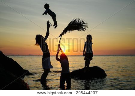 Silhouettes Of Mother With Three Children Standing In Water On The Calm Sea Beach At Sunset. Mother 