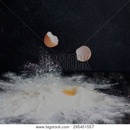 Eggs Are Broken And Fall Into Flour On A Black Background.
