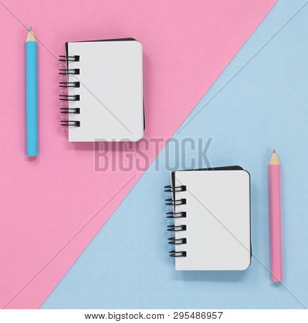 Two Open Notebooks On A Pink And Blue Diagonal Background, With A Coloured Pencils