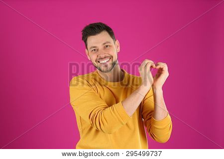 Portrait Of Handsome Man Making Heart With His Hands On Color Background