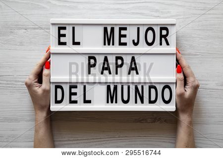 Female Hands Hold Lightbox With 'el Mejor Papa Del Mundo' Words Over White Wooden Background. Overhe