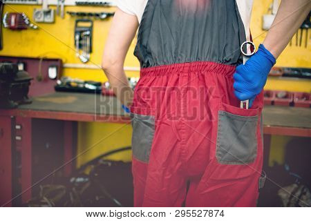 Female Car Mechanic Picking A Wrench From The Back Pocket Of Her Overalls In A Car Garage.  Gender E