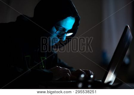 Hooded computer hacker stealing information with laptop