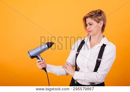 Pretty Young Woman Looking Confused At Her Hair Drayer Over Yellow Background.