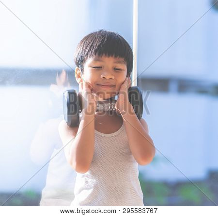 Little Boy Is Working Out With Dumbbell By The Windows City.