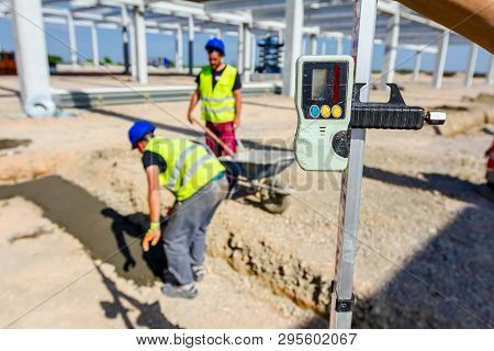 Construction Worker Is Holding Leveling Rod To Help Surveyor, Geodesist To Measure Position, Depth.