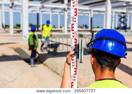Construction Worker Is Holding Leveling Rod To Help Surveyor, Geodesist To Measure Position, Depth.