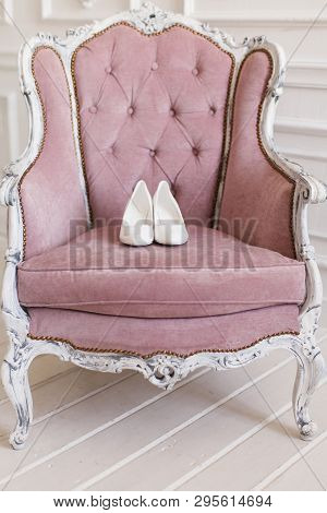 White Wedding Shoes Stand On The Seat Of A Pink Armchair With A Carved Back, Armrests And Legs.