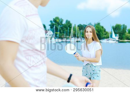 Male Is Holding Blue Ball, His Smiling Girlfriend Ready To Catch With Racket On Background. Young Ma