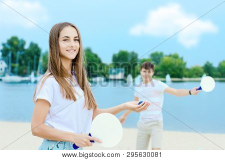 Young Smiling Woman In Light Clothes Is Holding White Racket And Ball In Her Hands. Cheerful Female 
