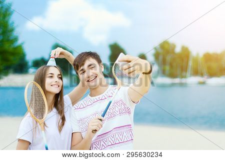 Young Smiling Woman In Light Clothes Is Holding White Racket And Ball In Her Hands. Cheerful Female 