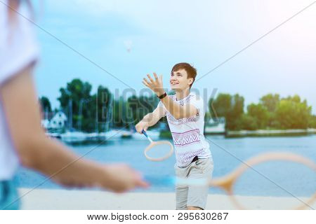Young Smiling Woman In Light Clothes Is Holding White Racket And Ball In Her Hands. Cheerful Female 