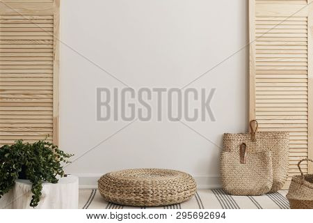 Empty White Wall Between Wooden Screen In Bright Interior With Wicker Pouf And Straw Bags