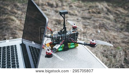 Fpv Drone Lies On The Table Near The Laptop And Control Panel. The Pilot Sets Up His Racing Drone Be