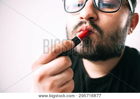 A Man In Glasses With A Beard Paints His Lips With Red Lipstick