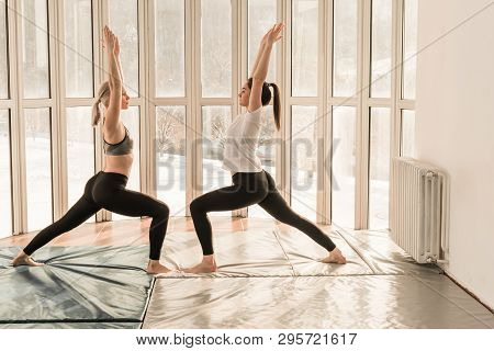 Two Beautiful Girls Practicing Yoga. Warrior Pose - Virabhadrasana. Yoga Concept, Healthy Lifestyle