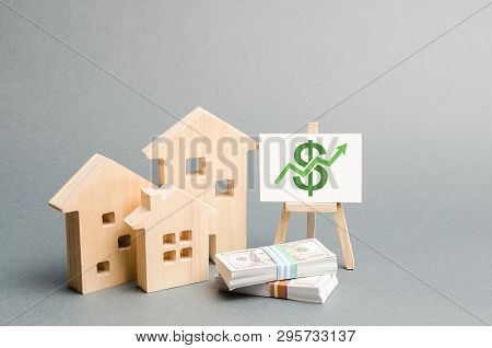Wooden Figures Of Houses And A Poster With Money. The Concept Of Real Estate Value Growth. Increase 