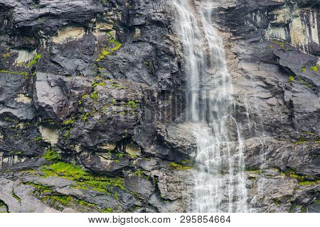 Waterfall On The Background Of The Rock Close-up. Rocky Textural Background With A Waterfall. Mounta