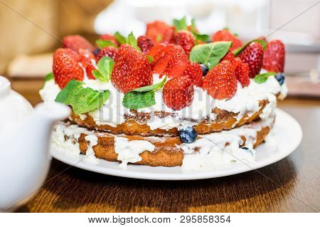 Strawberry Cake In Cream And Mint Leaves On The Table In A Plate, On The Background Of A Teapot With