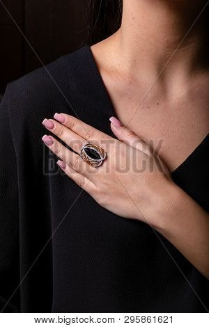 Womens Gold Ring With A Black Stone In The Middle On Finger, On A Black Background.