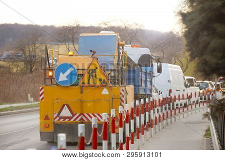 An Orange Street-cleaning Machine Stands In A Traffic Jam Near The Sidewalk Designated By Signal Bar