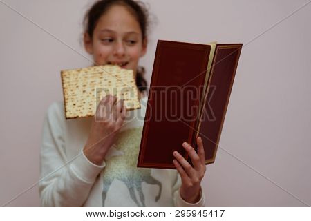 Portrait Of The Cute Teenager Girl Holding Matzah And Reads The Passover Haggadah. Jewish Child Eati