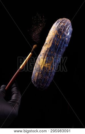 Beautiful Bright Eclair With Blets On A Dark Background. Hands Pastry Chef In Black Gloves.