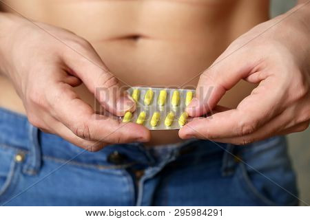 Man Taking Pills, Blister Pack With Yellow Capsules In Male Hands Close Up. Muscular Guy In Jeans Wi