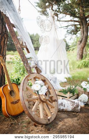 The Wheel, Guitar, Birch Logs Lie Near The Stairs Decorated With Lace Canvas In Nature. Green And Bl