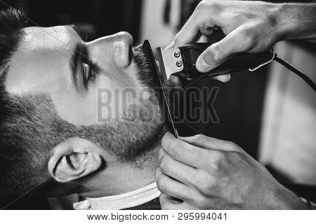 Client During Beard Shaving In Barbershop. Young Handsome Barber And Attractive Bearded Man. Black A