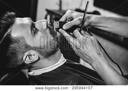 Client During Beard Shaving In Barbershop. Young Handsome Barber And Attractive Bearded Man. Black A