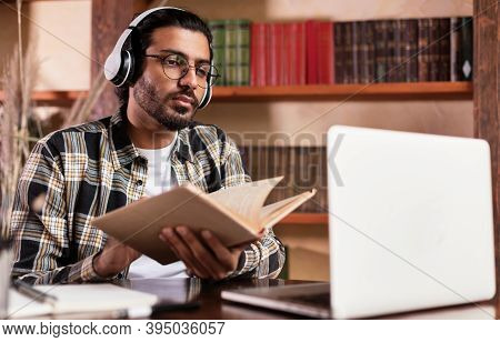 Indian Male Student At Laptop Learning Holding Book During Distant Lecture Webinar Via Video Call Si