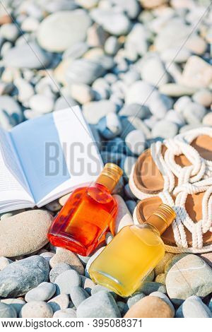 Beach Hat On Opened Book With Sunscreen And Shoes On Pebble Beach
